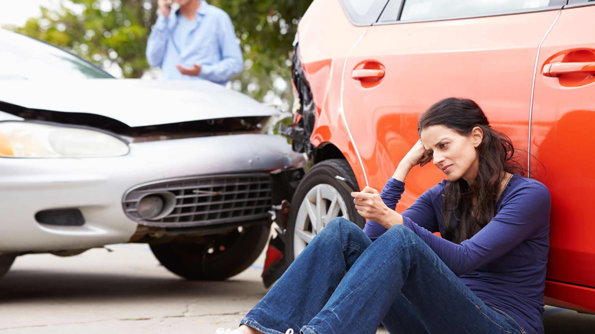 A woman sitting in front of her car after an accident.