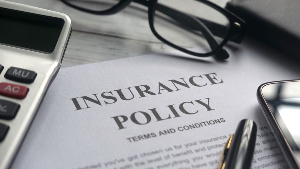 An insurance policy sheet with pens, glasses, and a calculator on top.