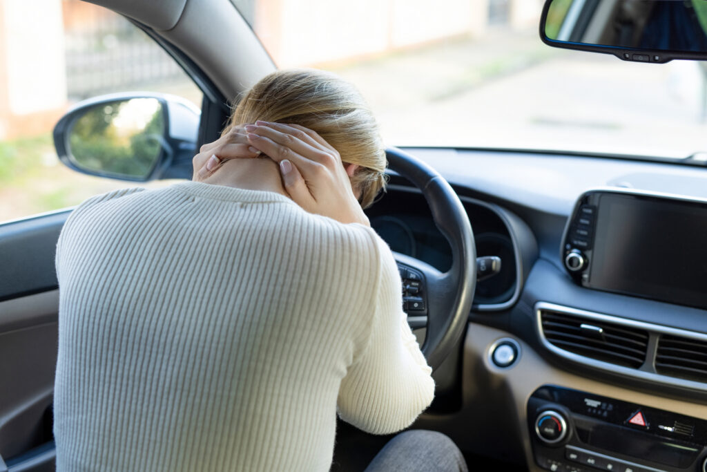 A blonde woman who is holding the back of her neck in pain.