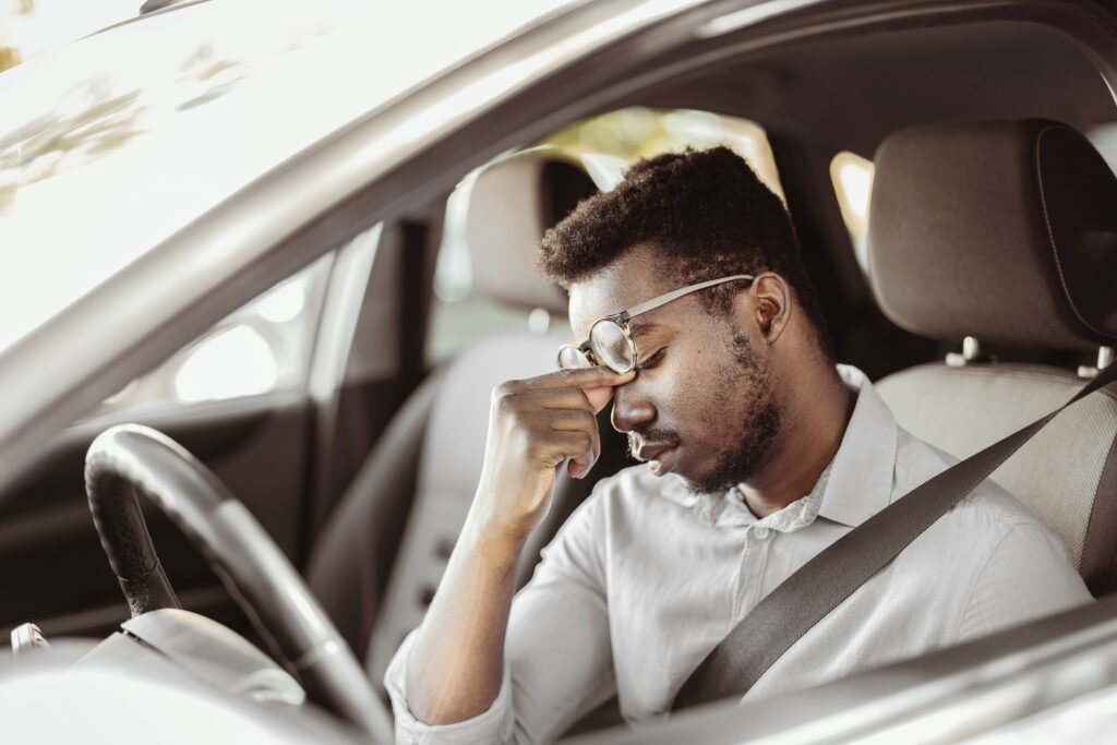 A tired man pinching his nose while behind the wheel.