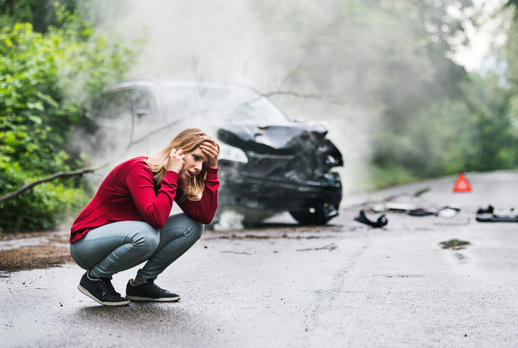 A woman kneeling on the ground panicking about a car accident.