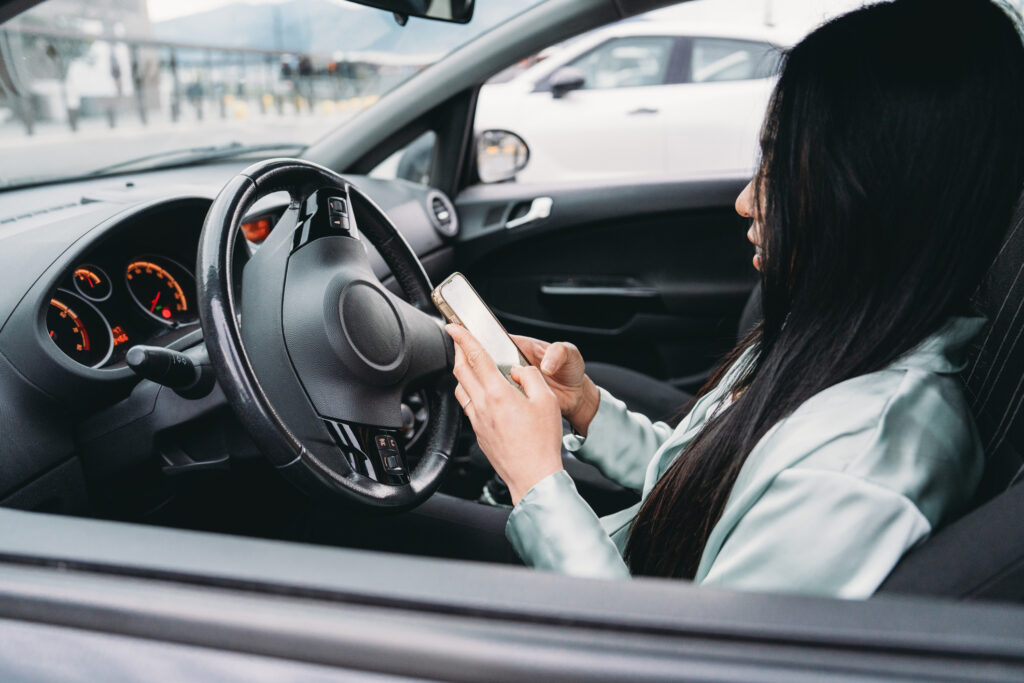 A woman texting and driving while behind the wheel.