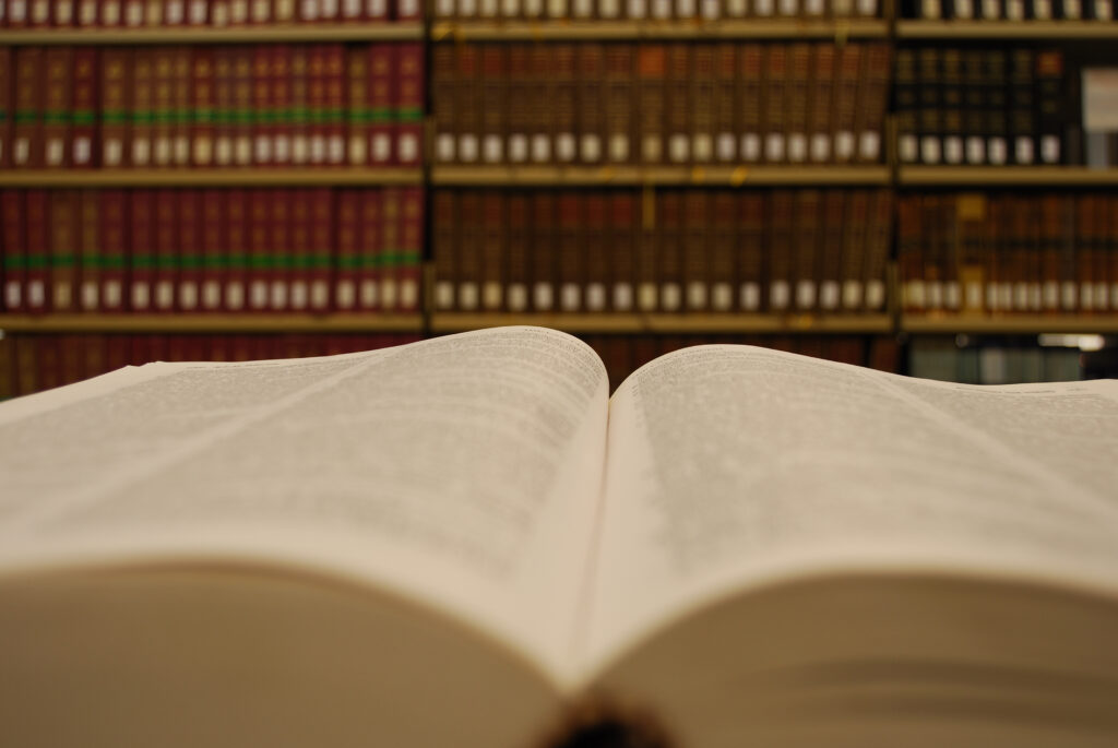An open book with a bookshelf of books in the background.
