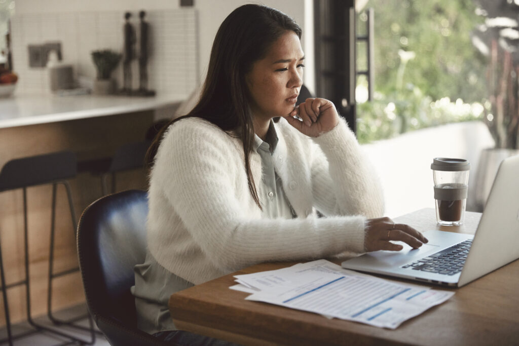 A woman calculating things while on the phone and looking on her computer.